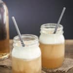 Jars of frozen butterbeer with gray straws sitting on a wood surface.