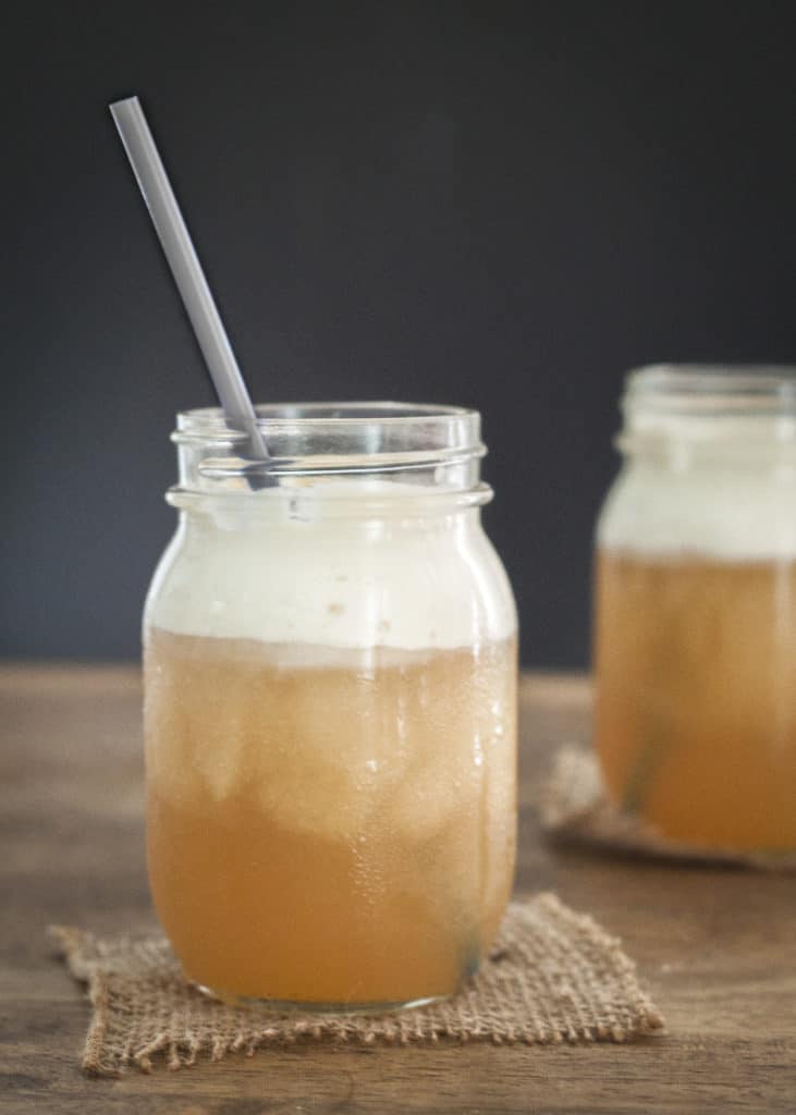 Jars of frozen butterbeer with gray straws sitting on a wood surface.