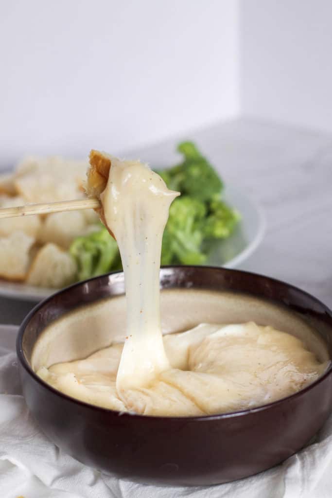 A bowl of cheese fondue with a cheese pull.
