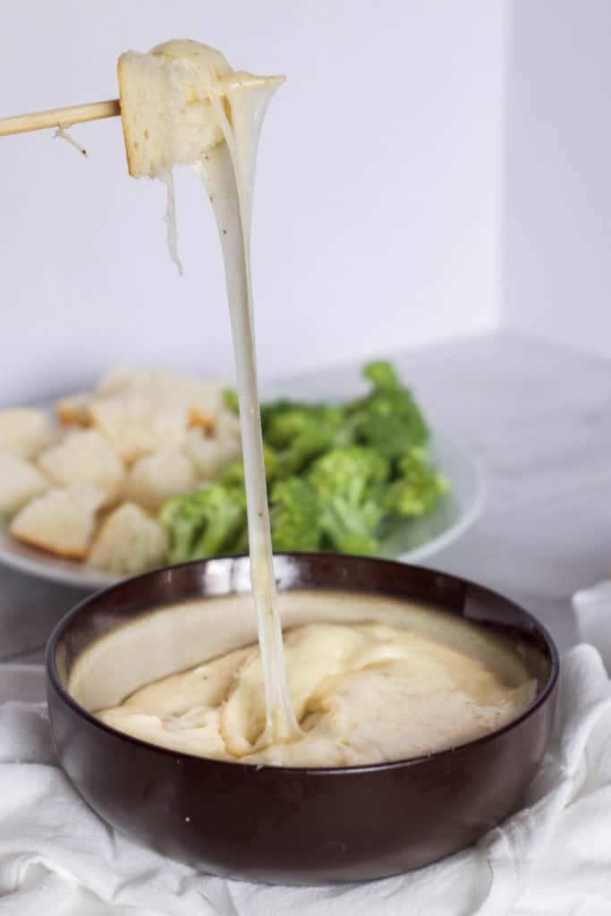 A bowl of cheese fondue on a white surface with a cheese pull.