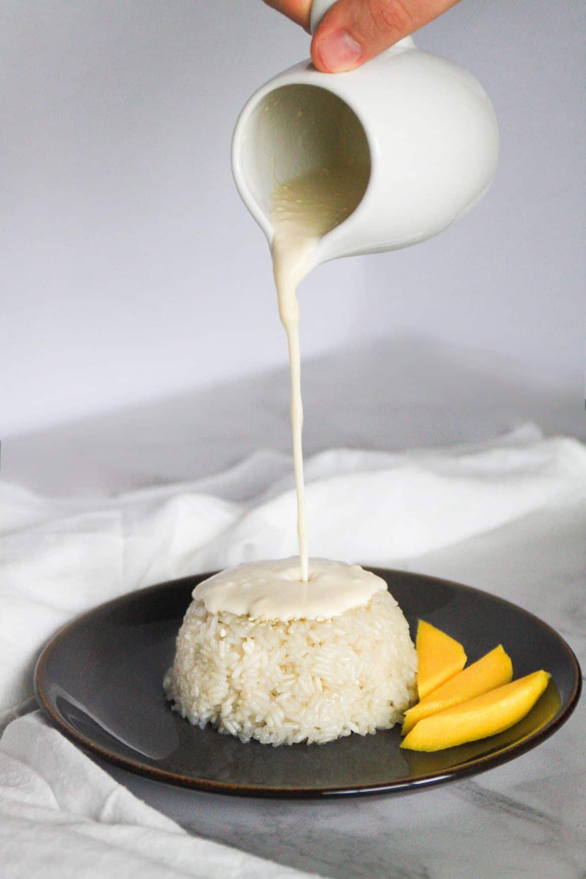Thai Mango Sticky Rice with a hand pouring sugar syrup on top.