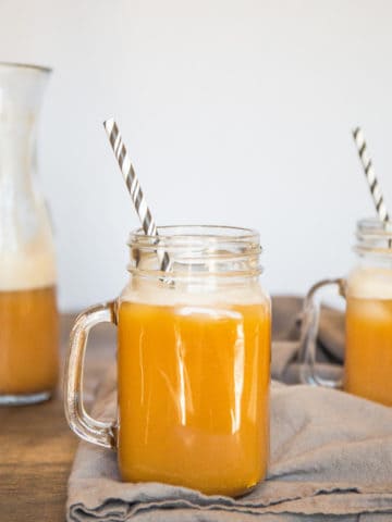 A glass of pumpkin juice with a striped straw on a wood surface.