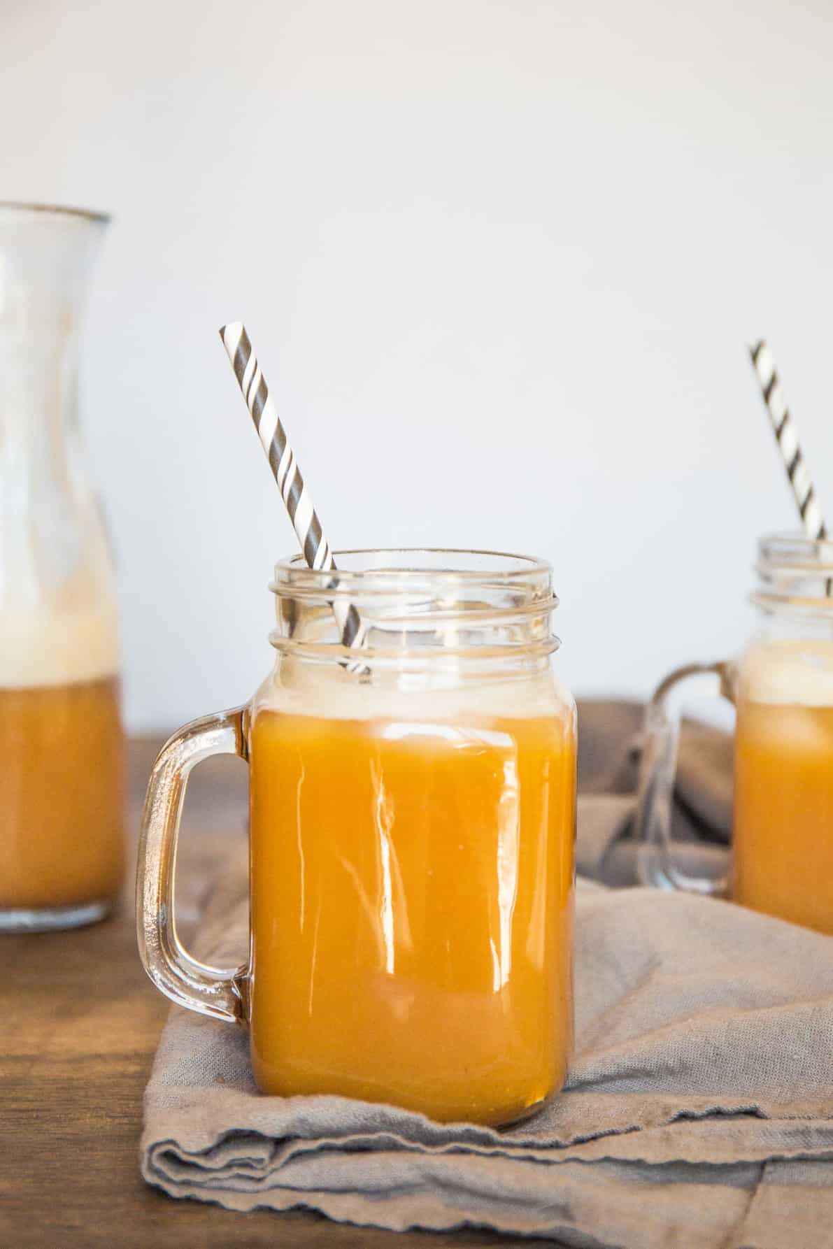 A glass of pumpkin juice with a striped straw on a wood surface.