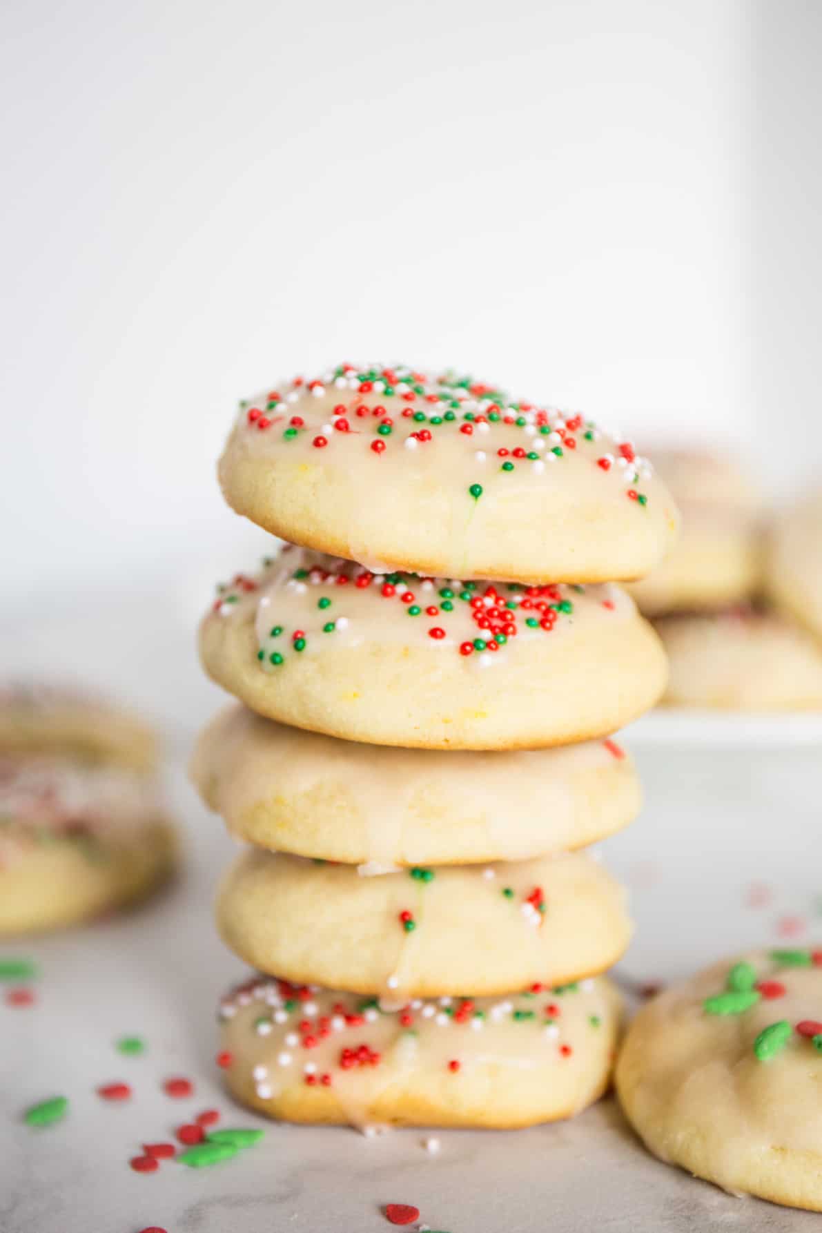 Italian ricotta cookies in a stack on a white surface.