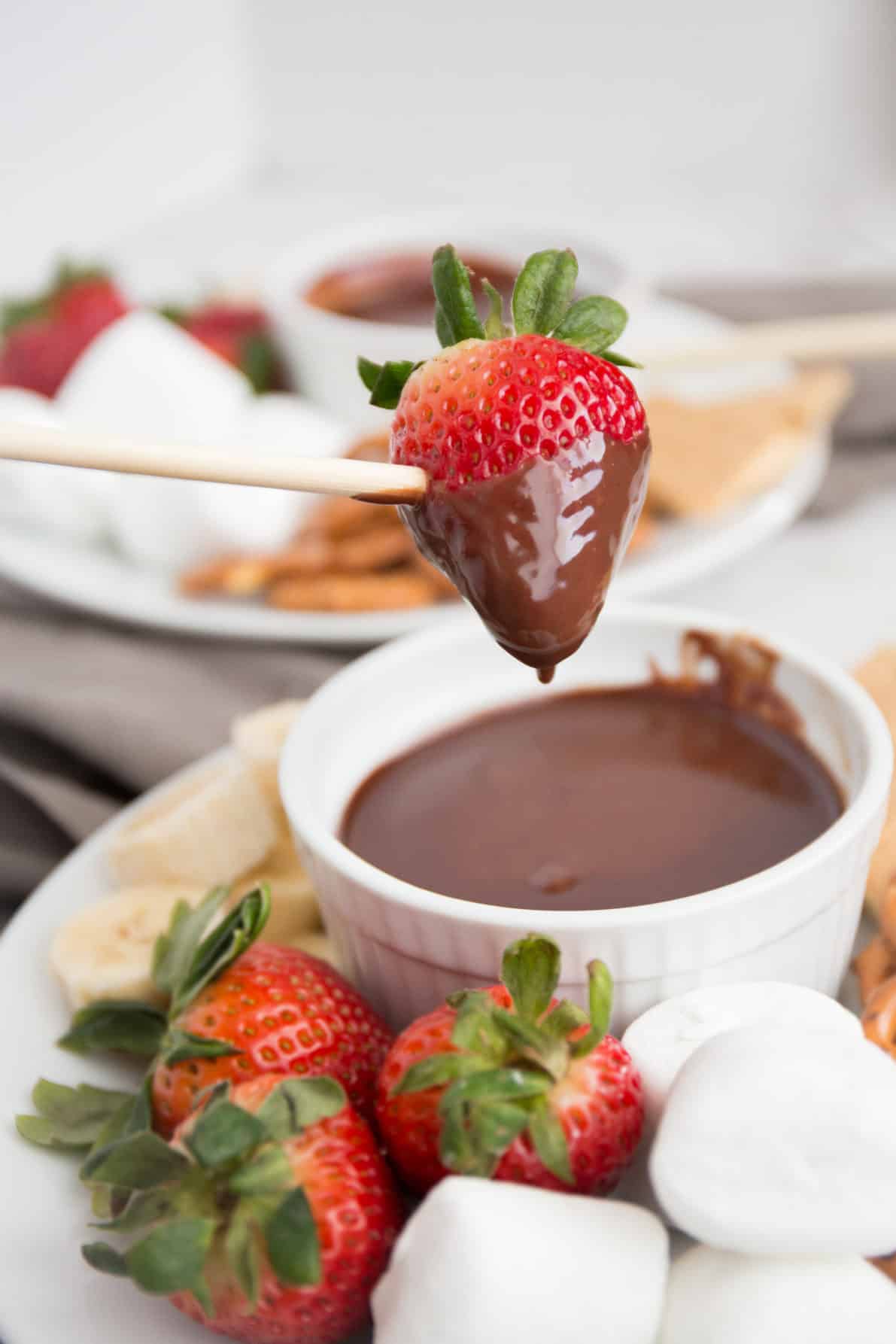 A bowl of chocolate fondue next to strawberries and marshmallows.