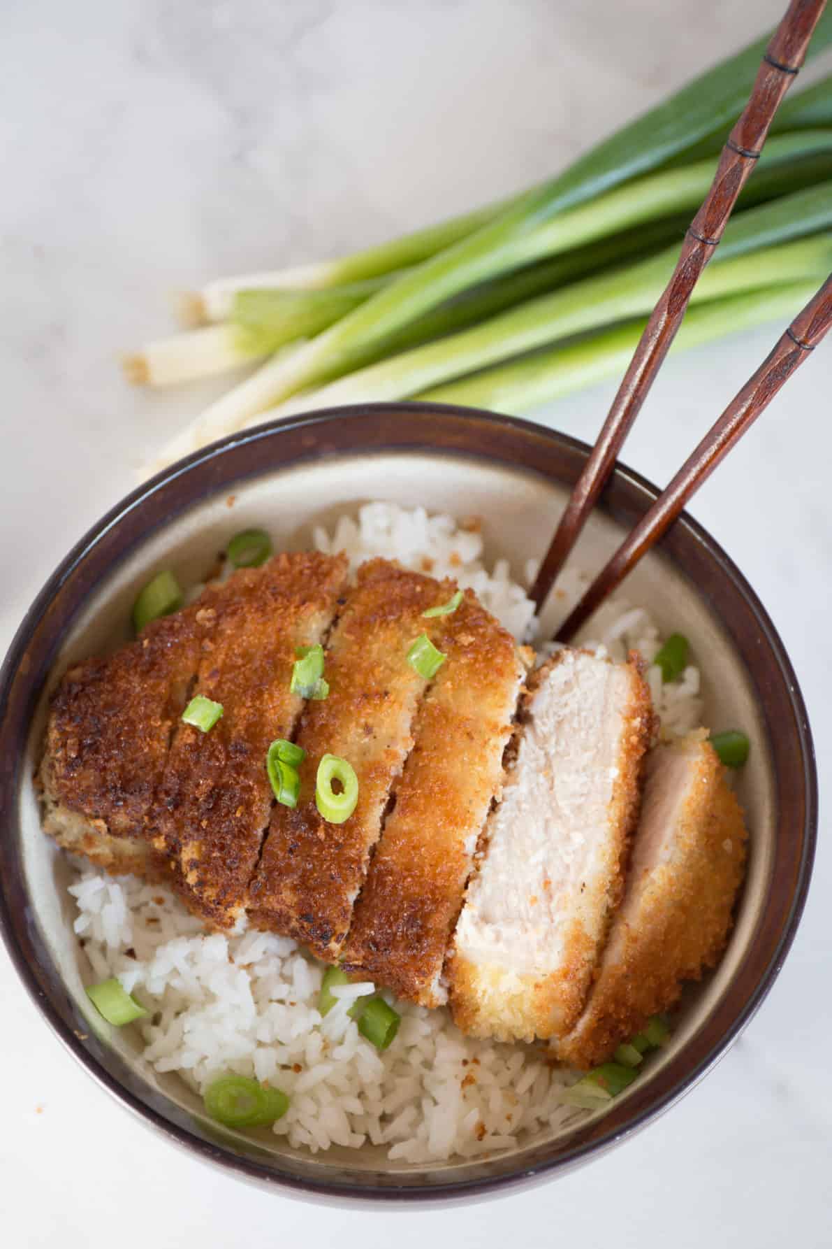 Japanese pork tonkatsu on a bed of rice in a bowl with chopsticks.