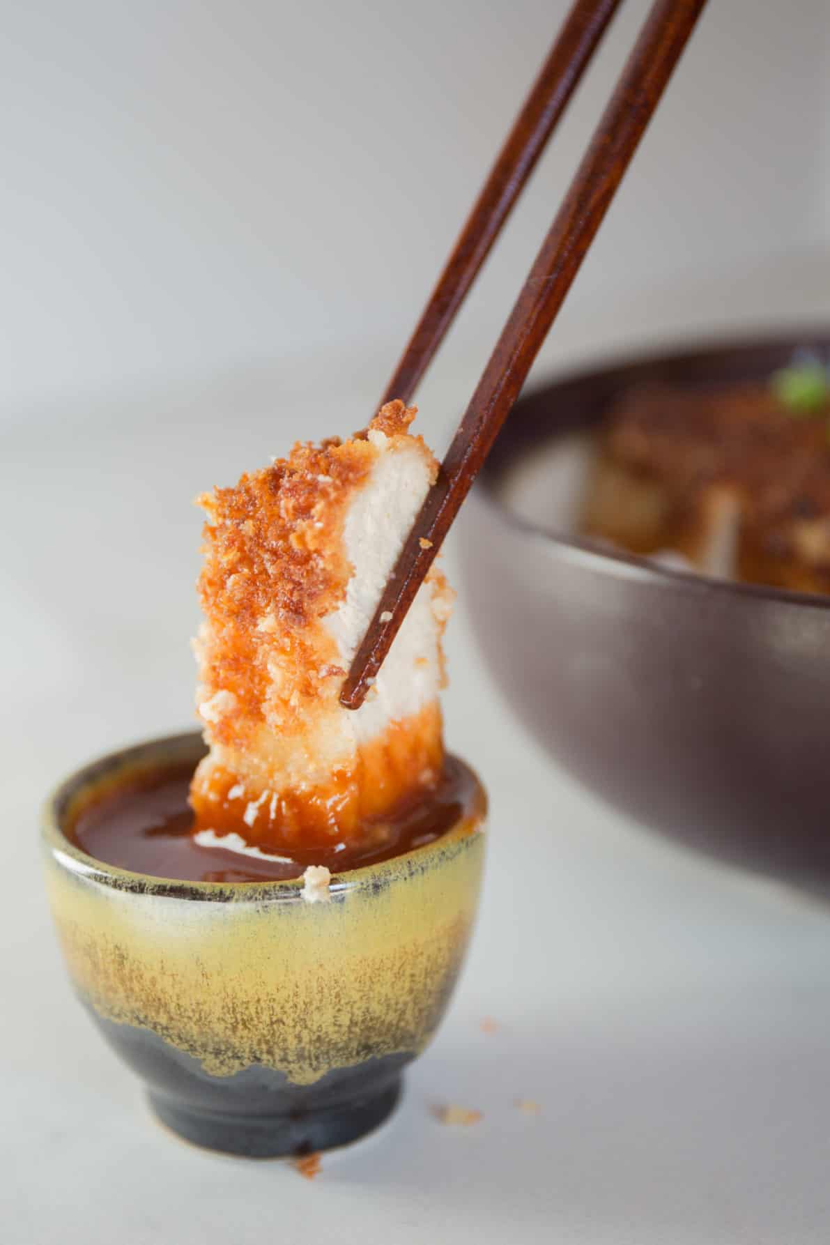 Japanese pork tonkatsu dipped in a sauce with chopsticks.