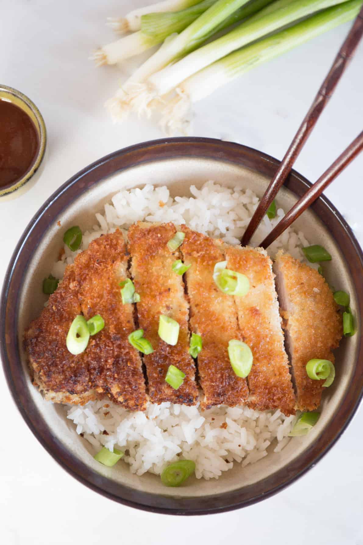 Japanese pork tonkatsu on a bed of rice in a bowl with chopsticks.