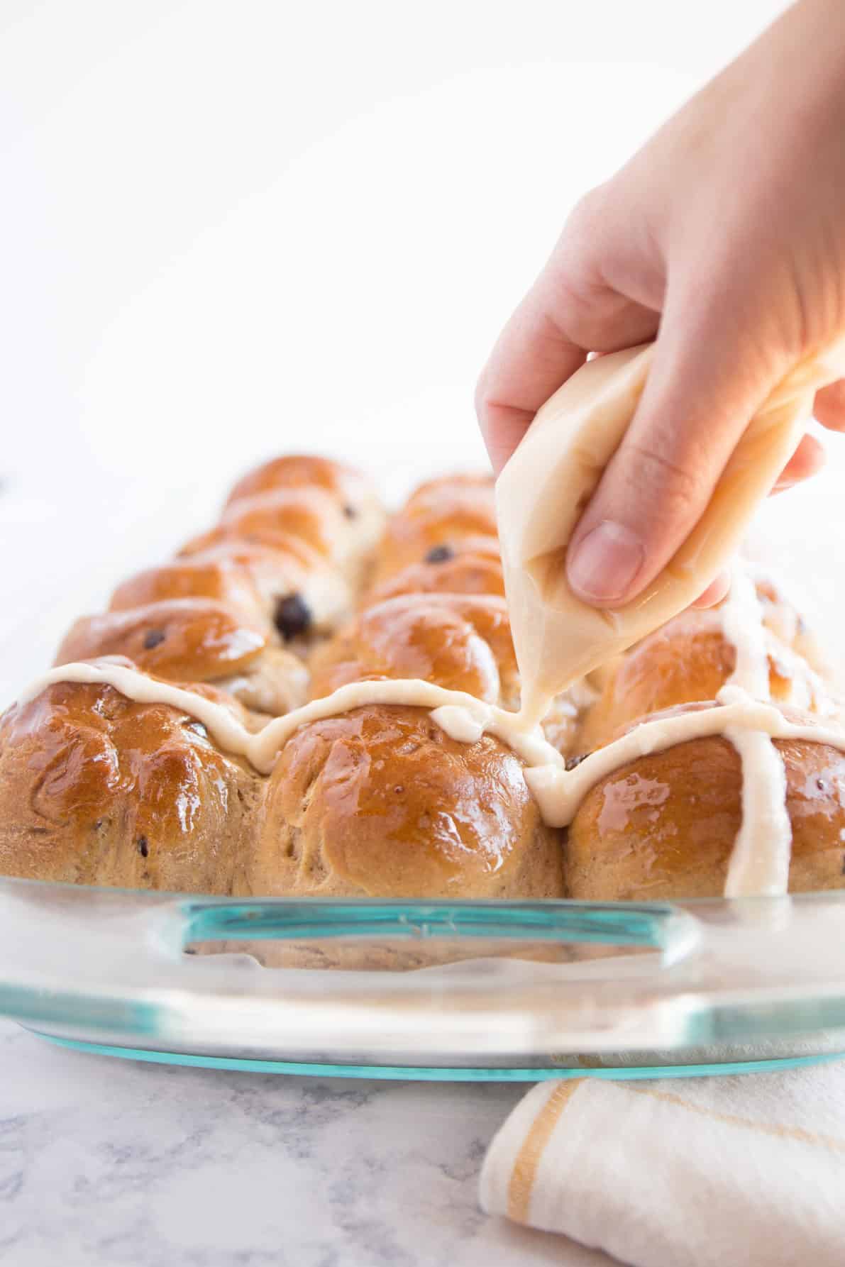 Hot Cross Buns that are being iced with cream cheese icing.