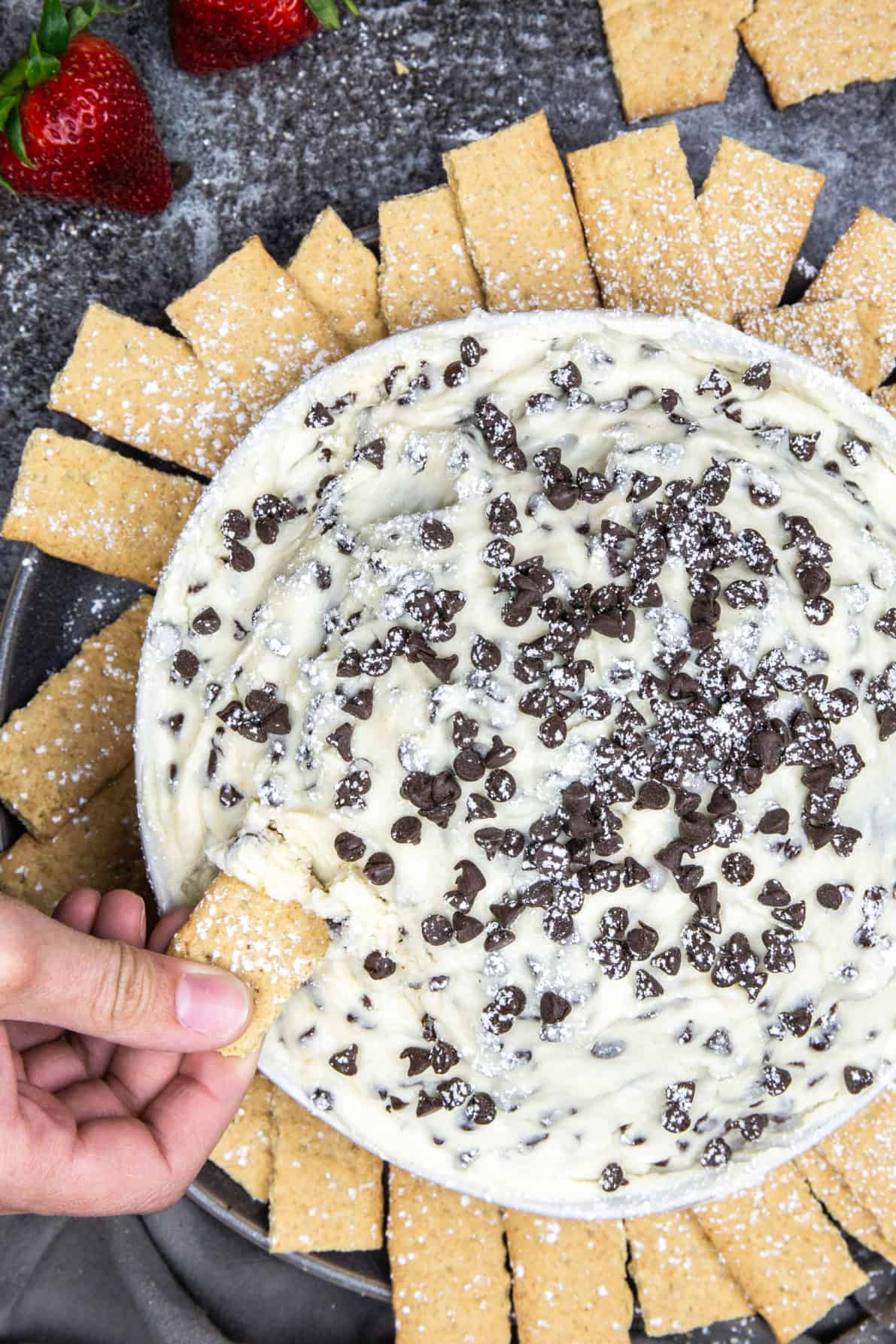 A photo of cannoli dip with a graham cracker being dipped in it.
