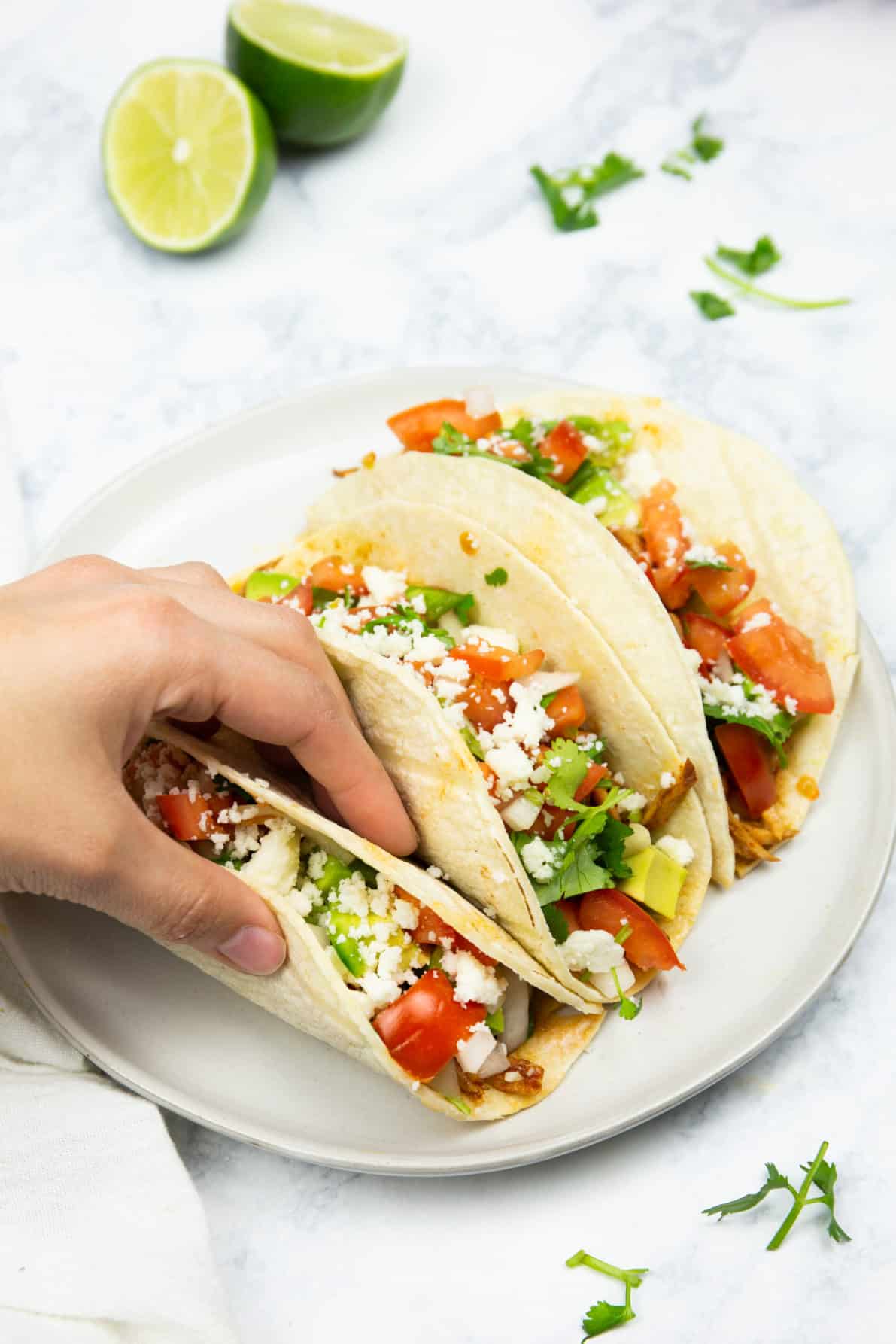 A hand grabbing a sweet pork taco from the plate.
