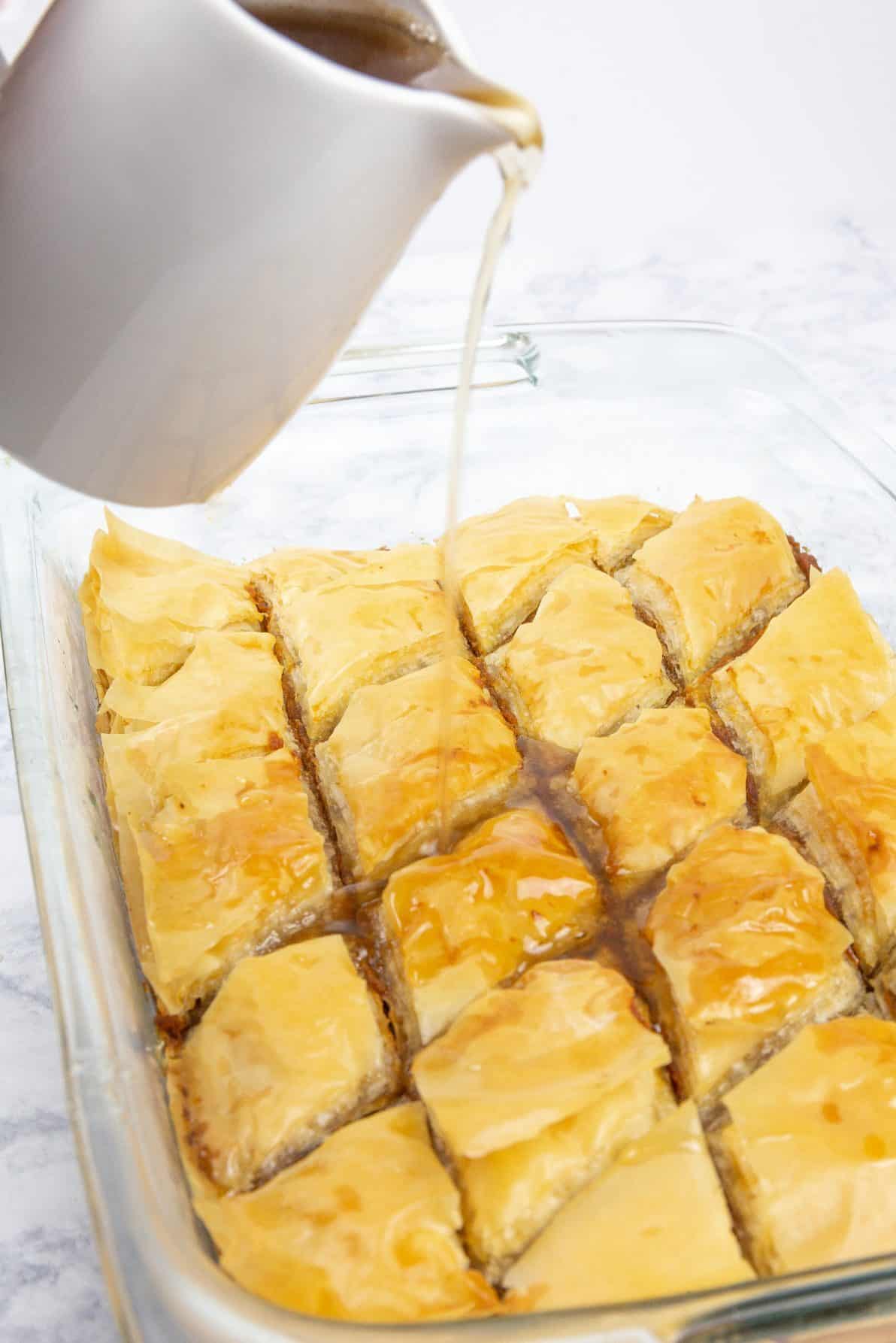 Pumpkin baklava in a pan with honey syrup being poured on top.