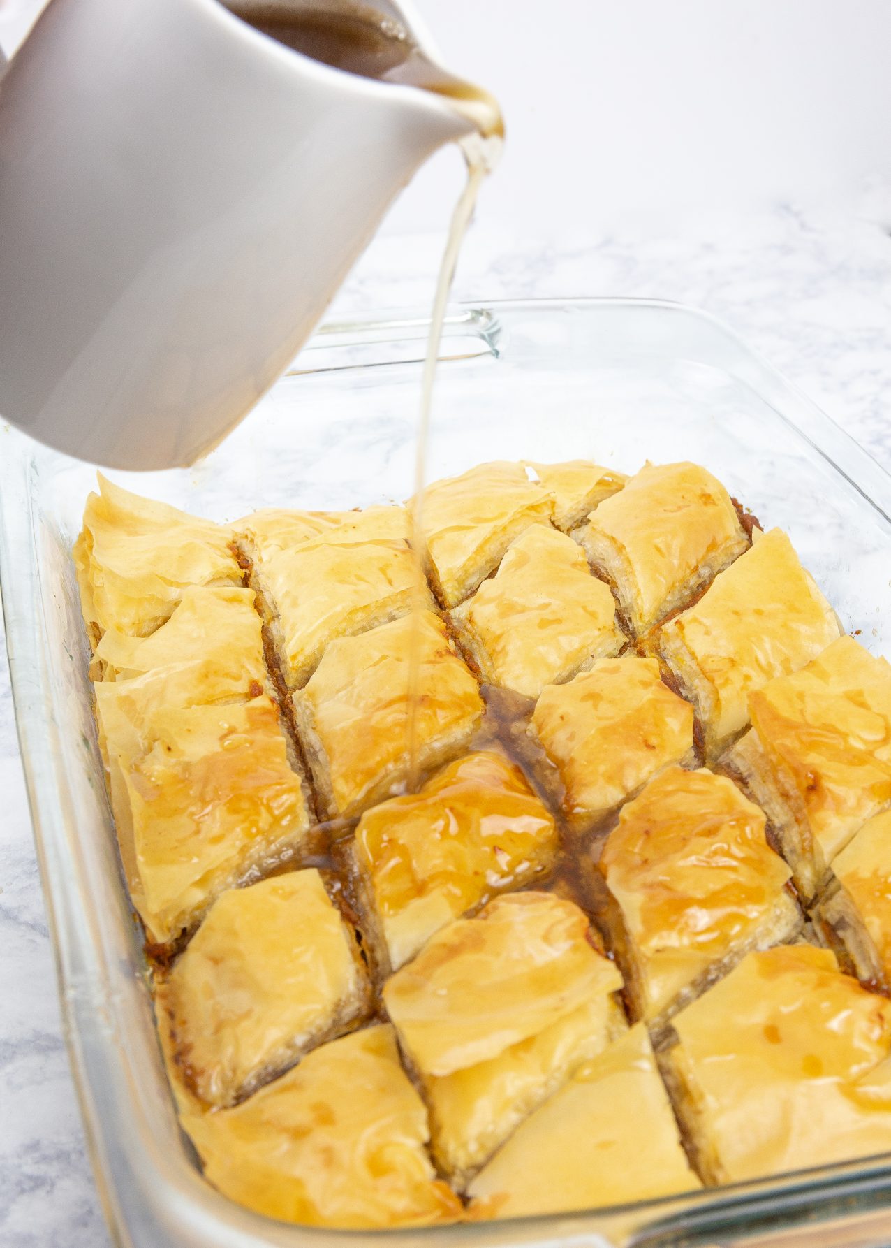 Pumpkin baklava in a pan with honey syrup being poured on top.