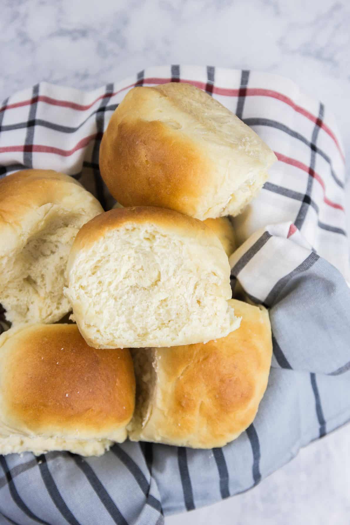 Milk bread rolls piled up in a bowl with a plaid towel.