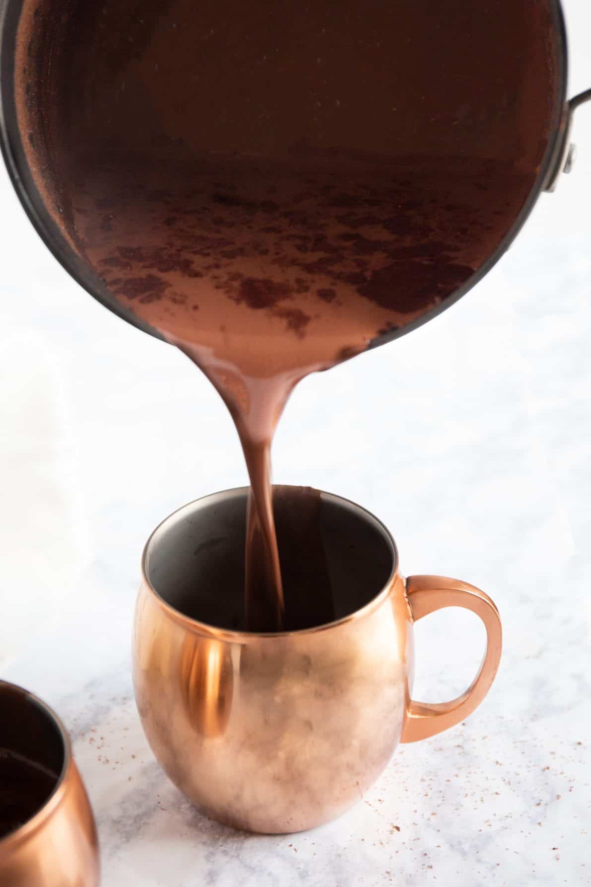 A saucepan filled with Mexican hot chocolate pouring into a copper mug.