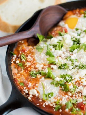 A cast iron skillet with shakshuka with feta and wooden spoon.
