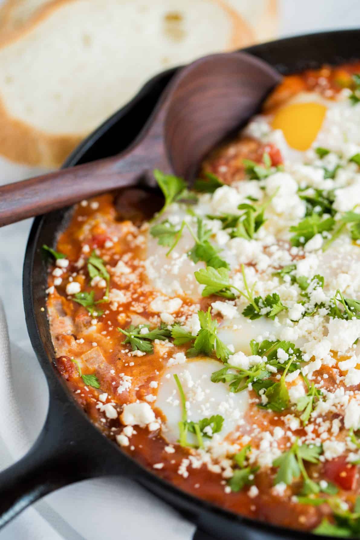 A cast iron skillet with shakshuka with feta and wooden spoon.