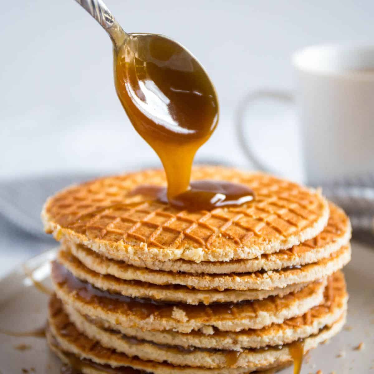 A stack of stroopwafels with a spoon drizzling caramel on top.