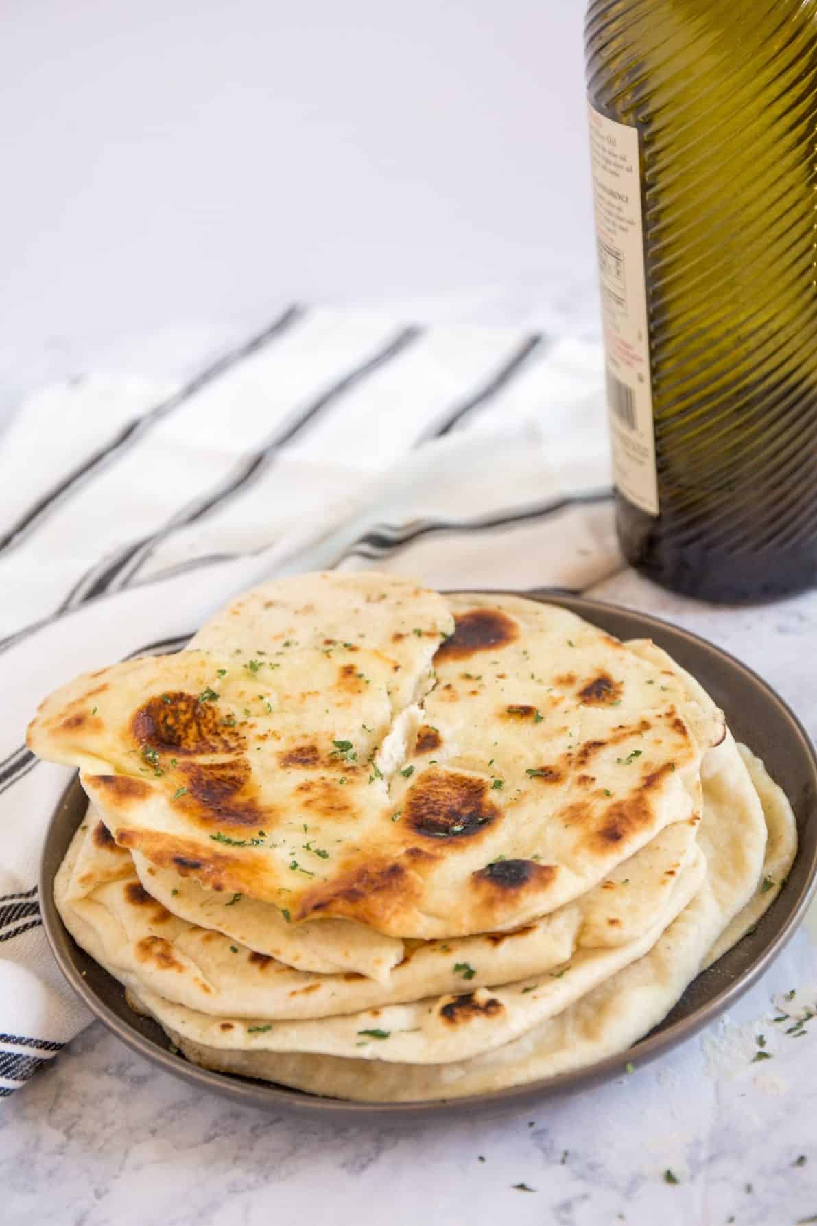 Pita bread on a plate next to a bottle of olive oil.