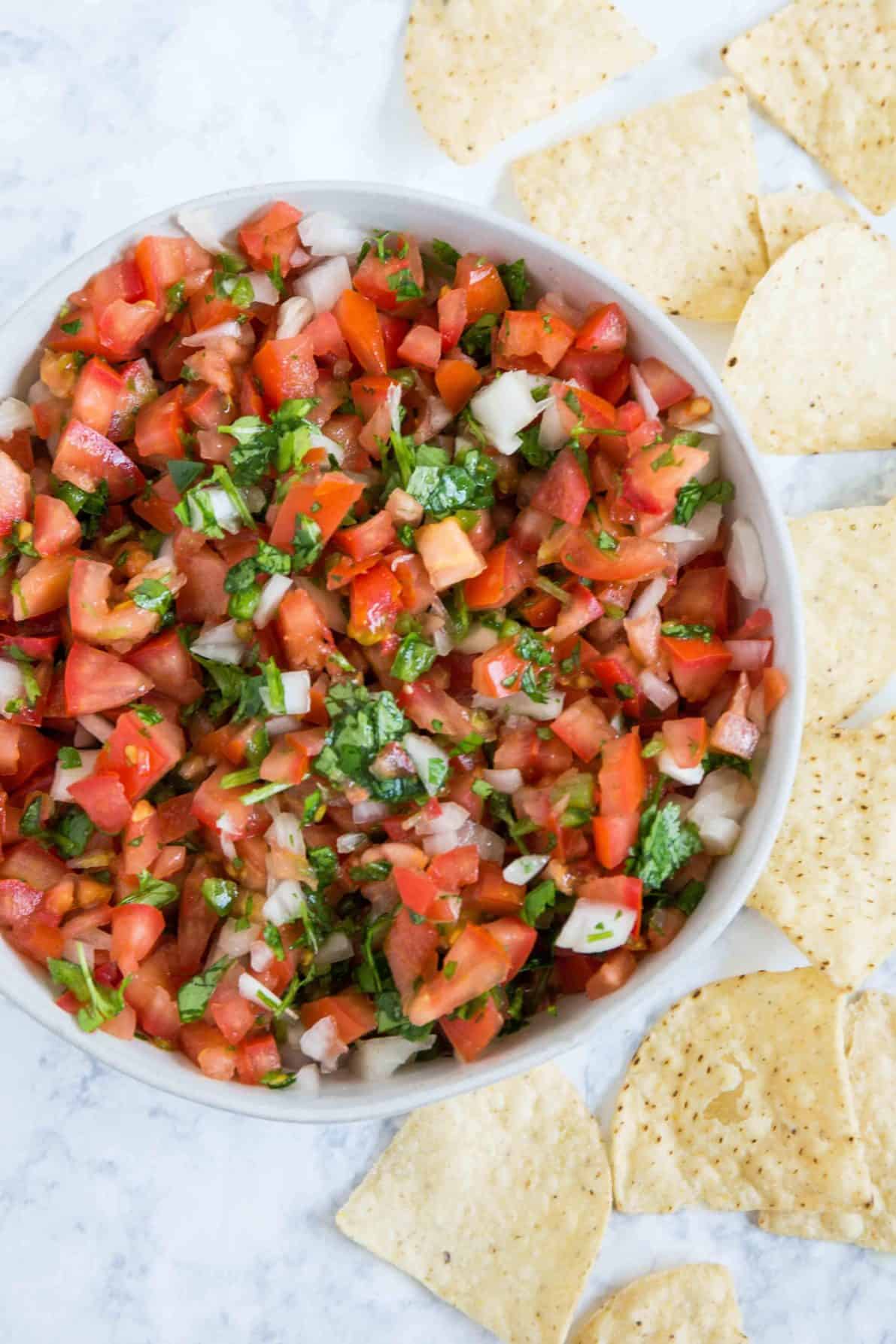 Pico de gallo in a bowl with chips around it.