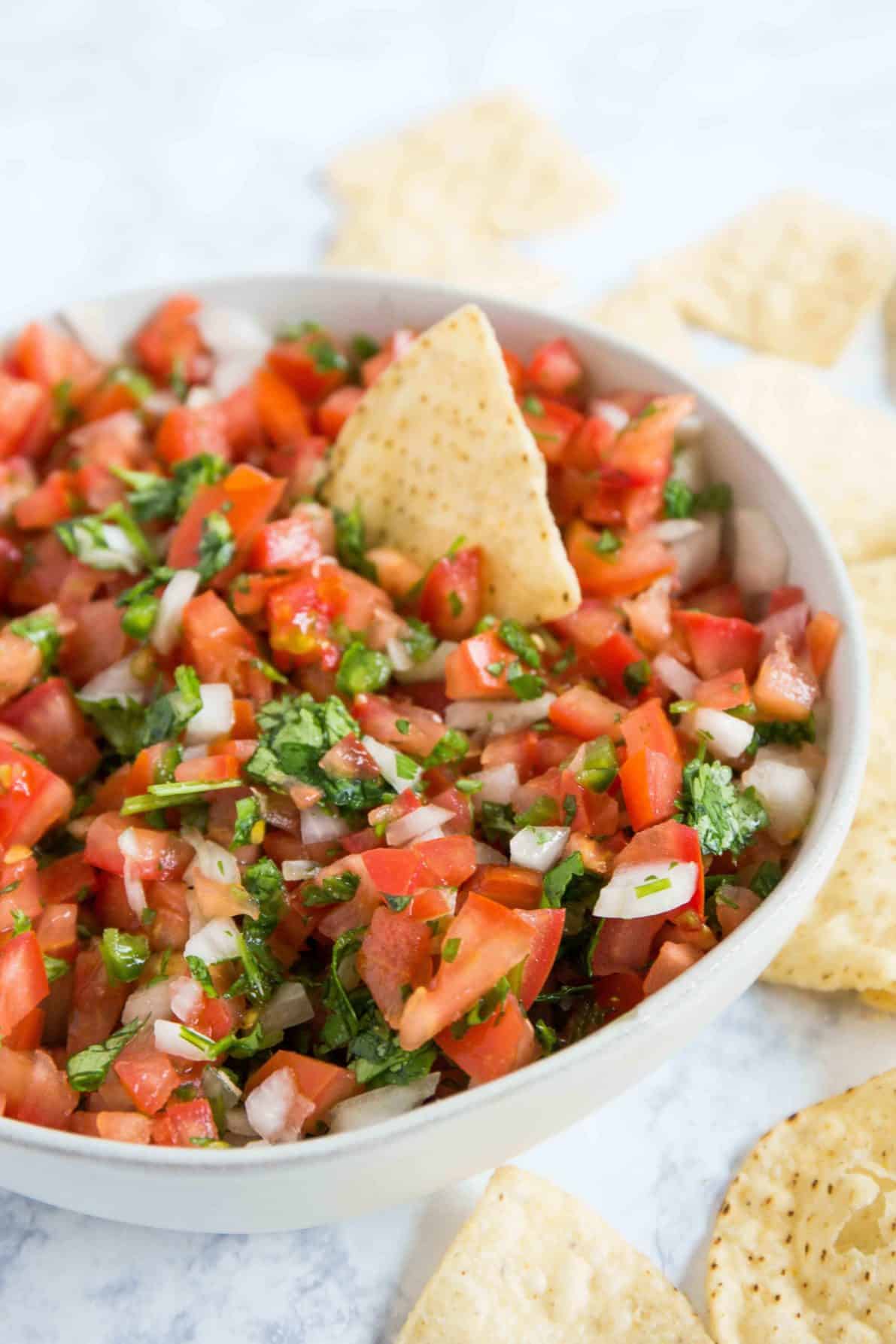 Pico de gallo in a bowl with chips around it.