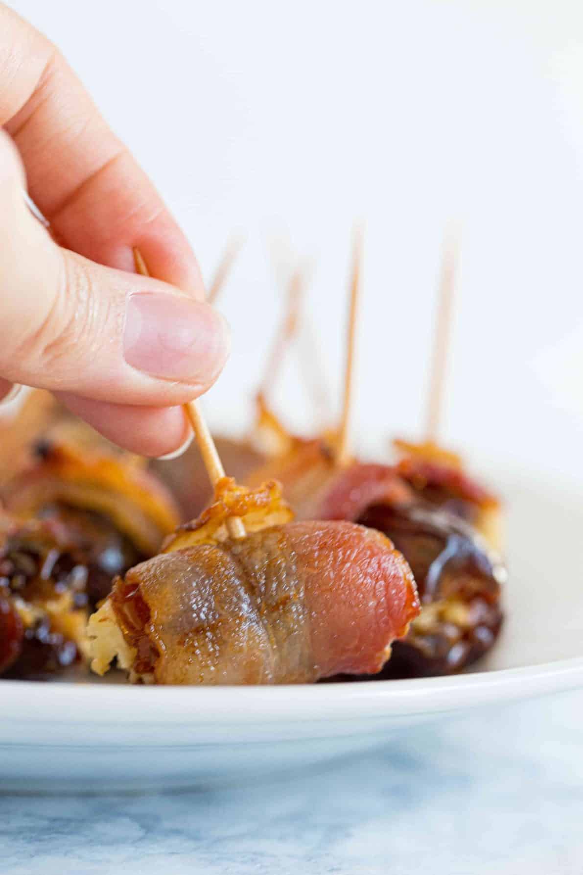 A plate of bacon wrapped dates with someone grabbing one.