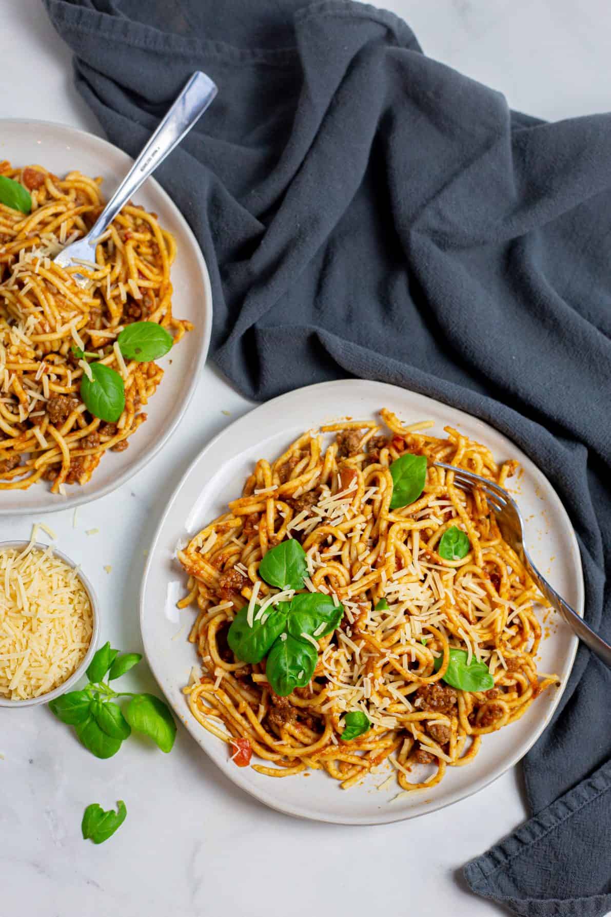 Two white plates of spaghetti next to a gray linen.