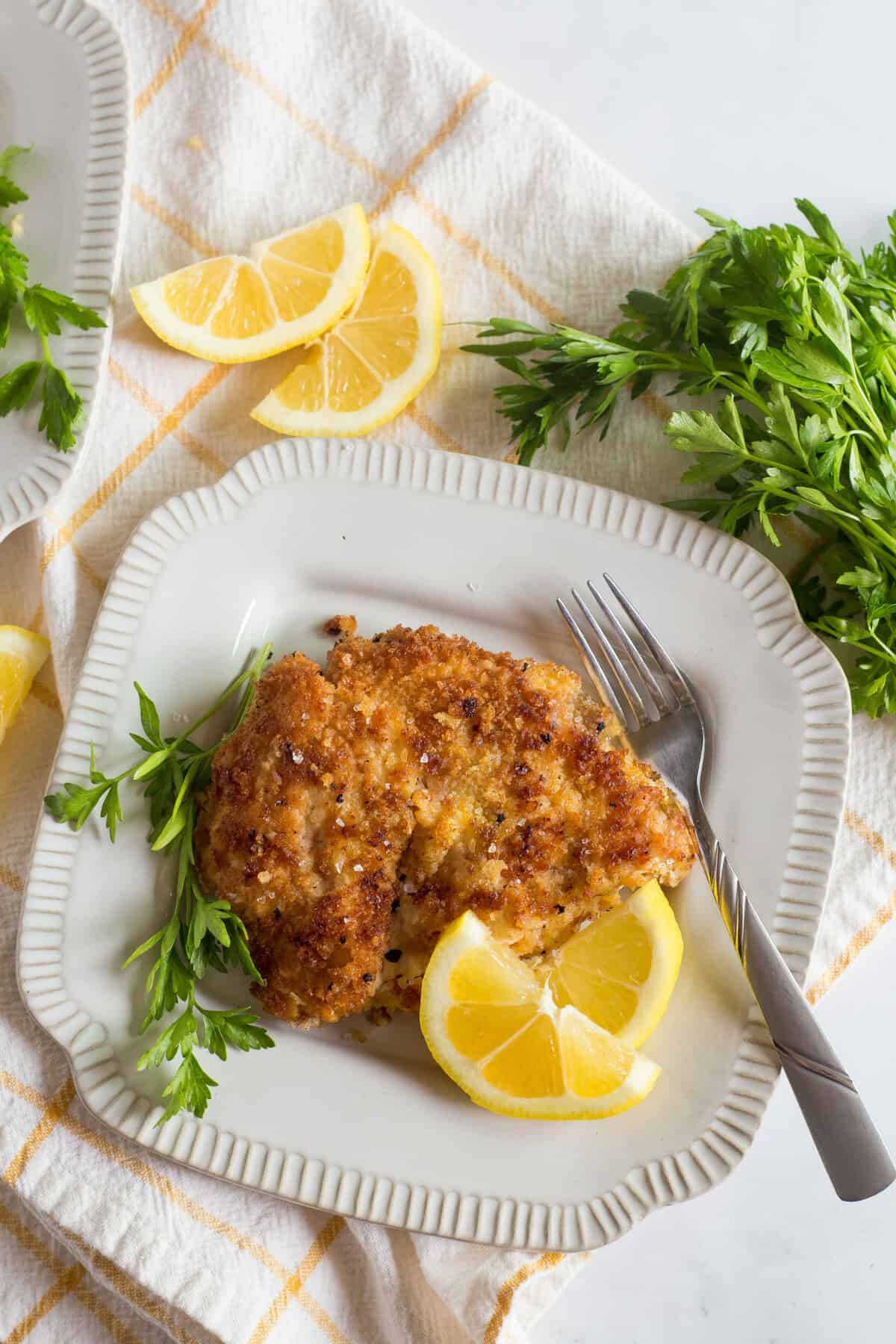 Chicken schnitzel with lemon wedges on a white plate.