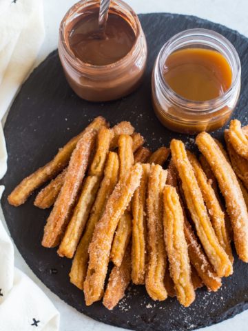 Mexican churros with dipping sauces laid on a piece of black slate.