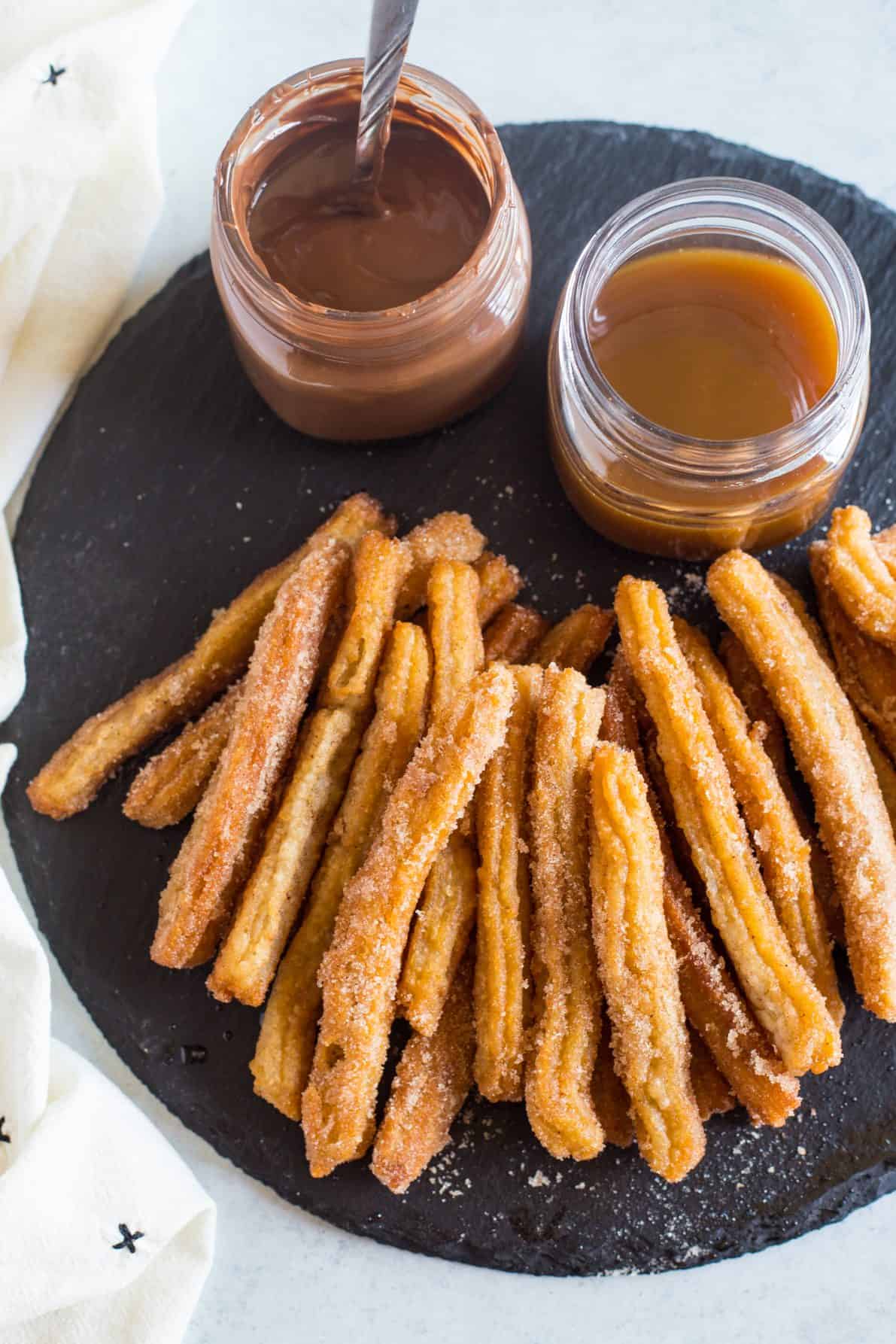 Mexican churros with dipping sauces laid on a piece of black slate.