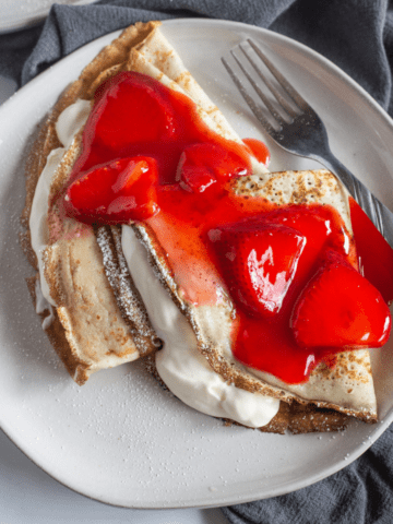 A white plate with strawberry crepes.
