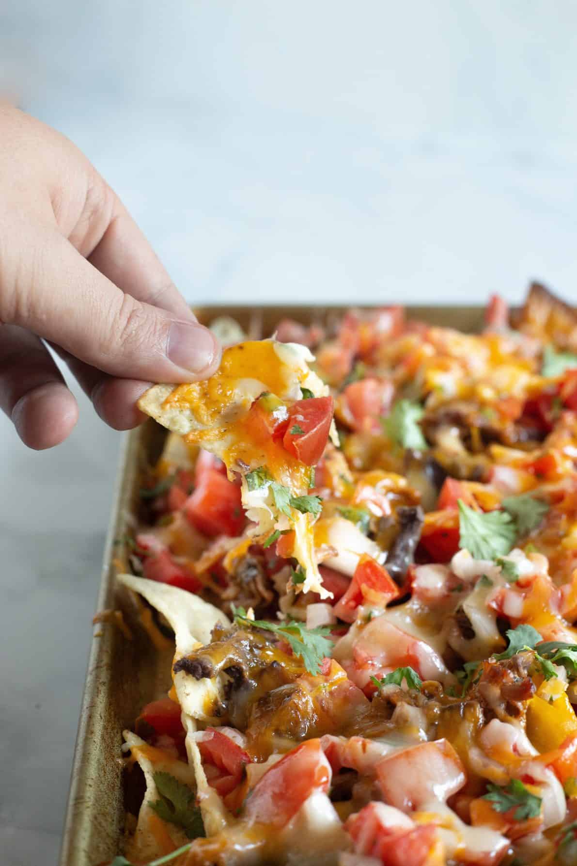 Sweet Pork Sheet Pan Nachos with a chip being pulled off.