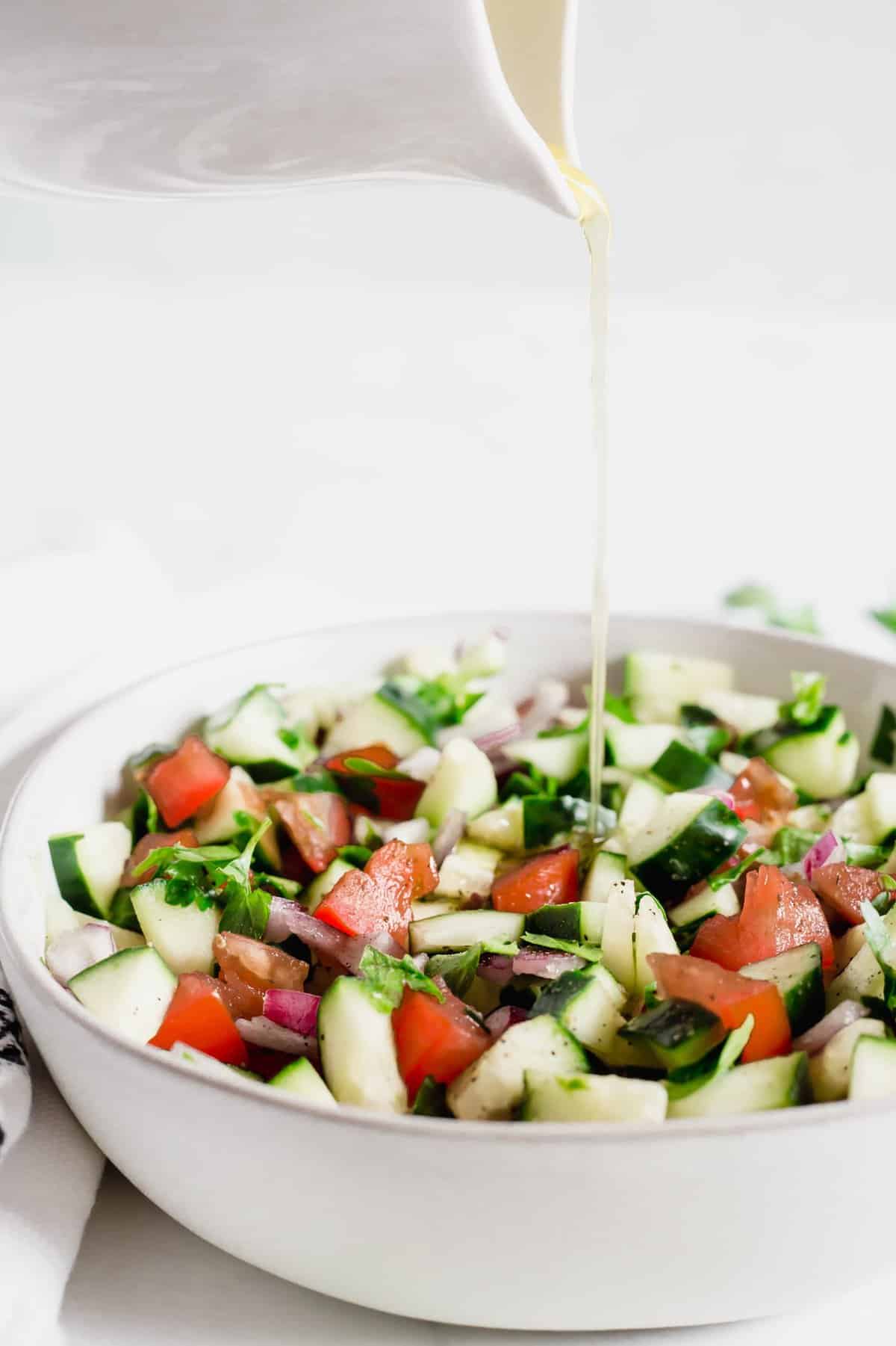 Egyptian Tomato and Cucumber Salad in a white bowl with dressing drizzling on top.