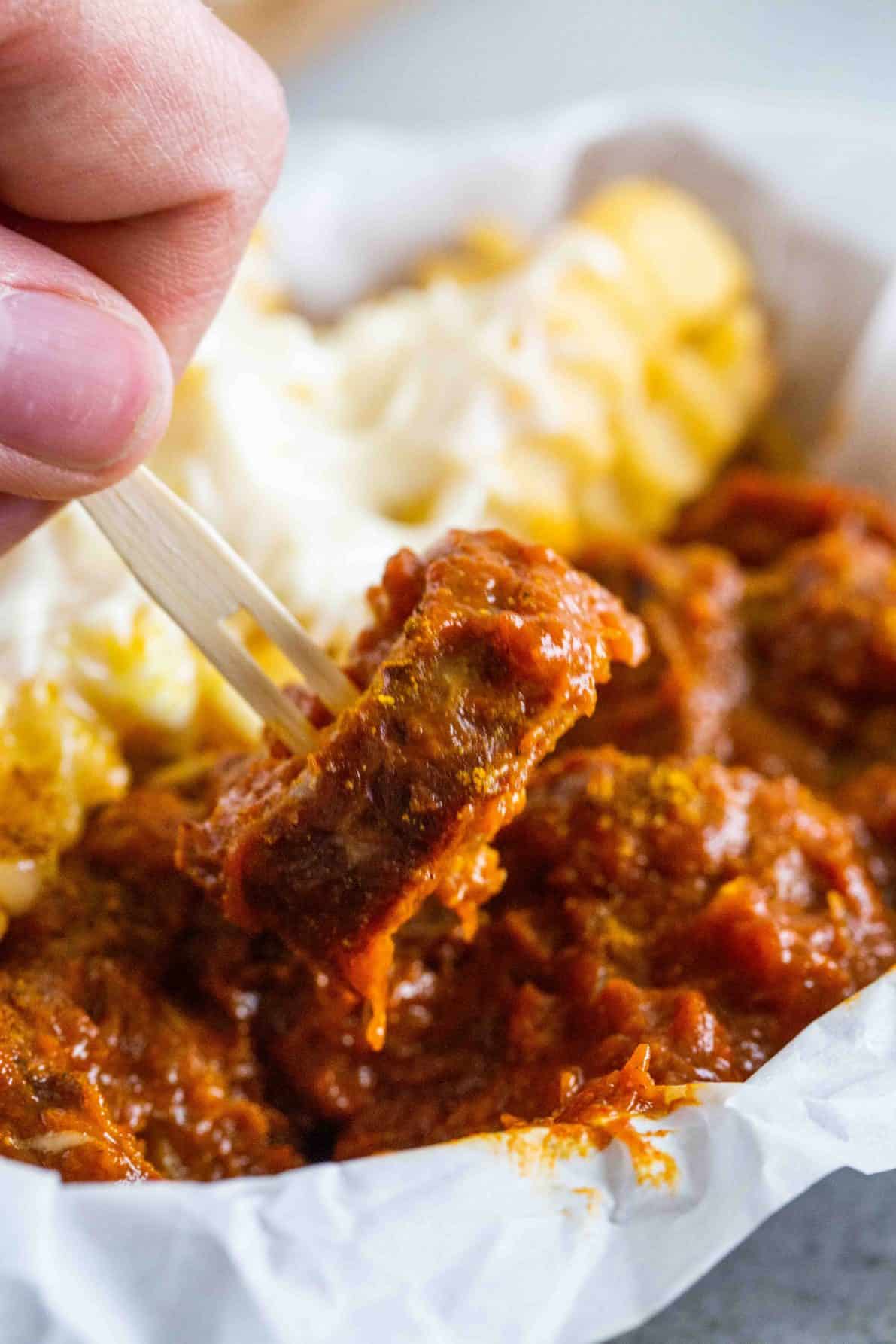 Hand holding up a piece of currywurst.