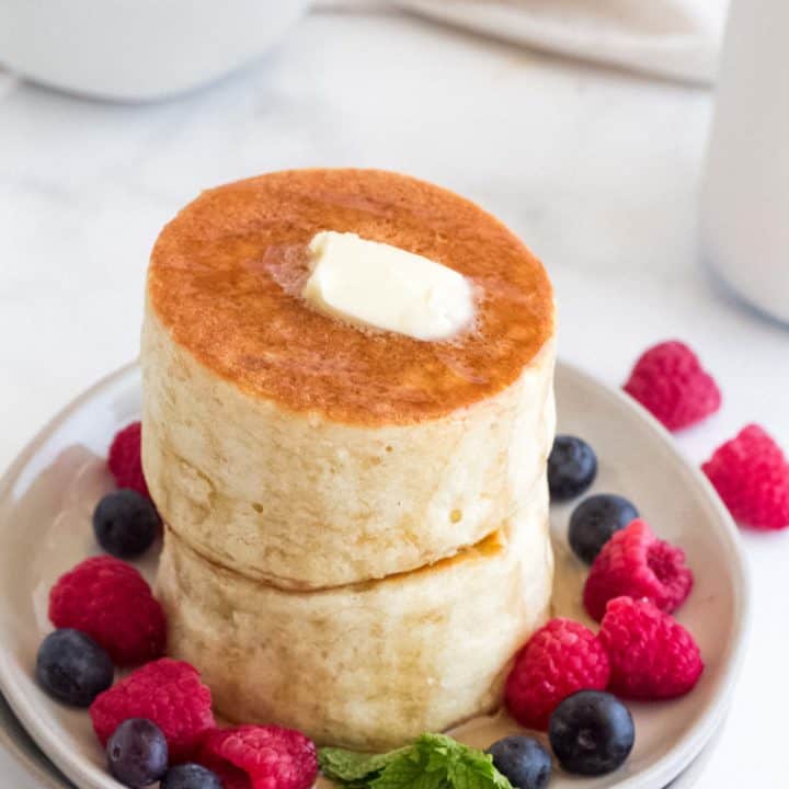 A stack of Japanese pancakes with berries on a white plate.