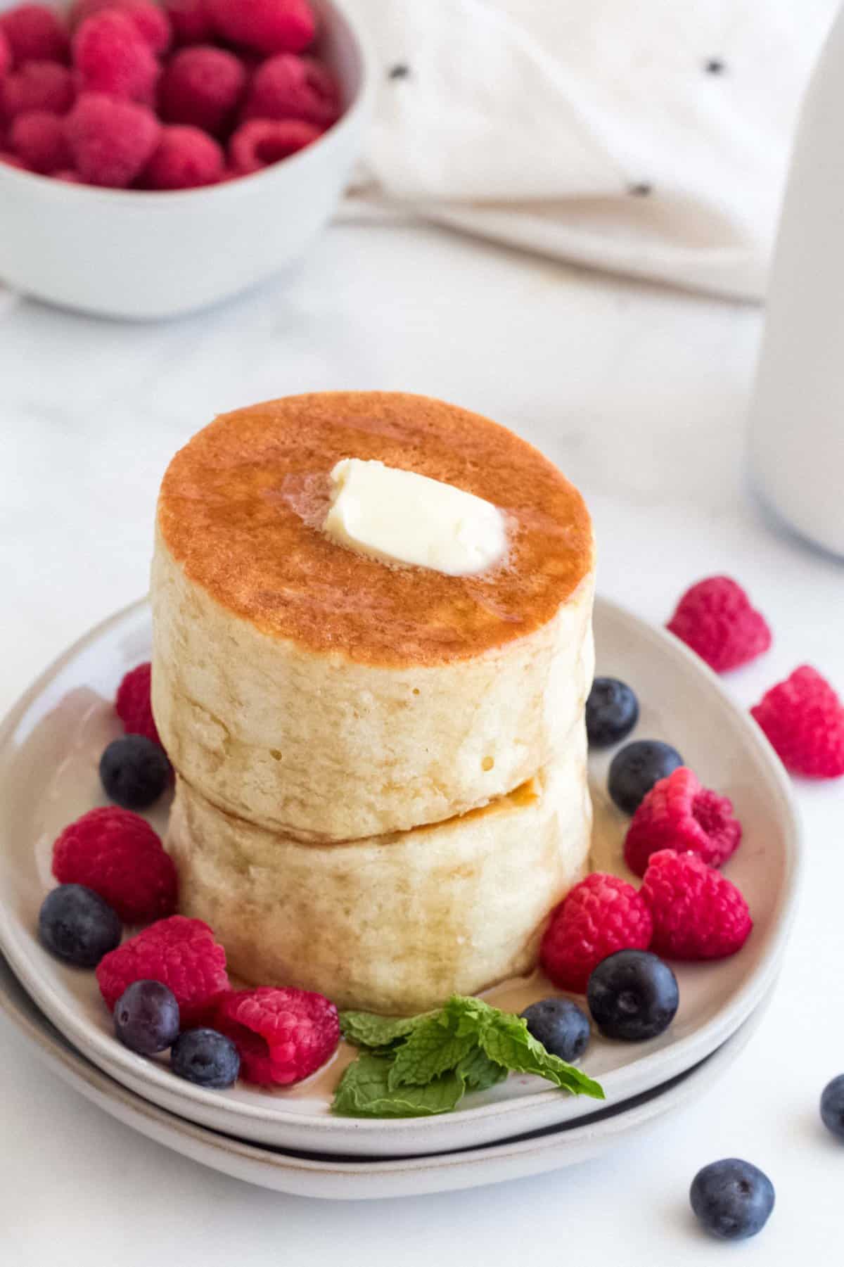 A stack of Japanese pancakes with berries on a white plate.
