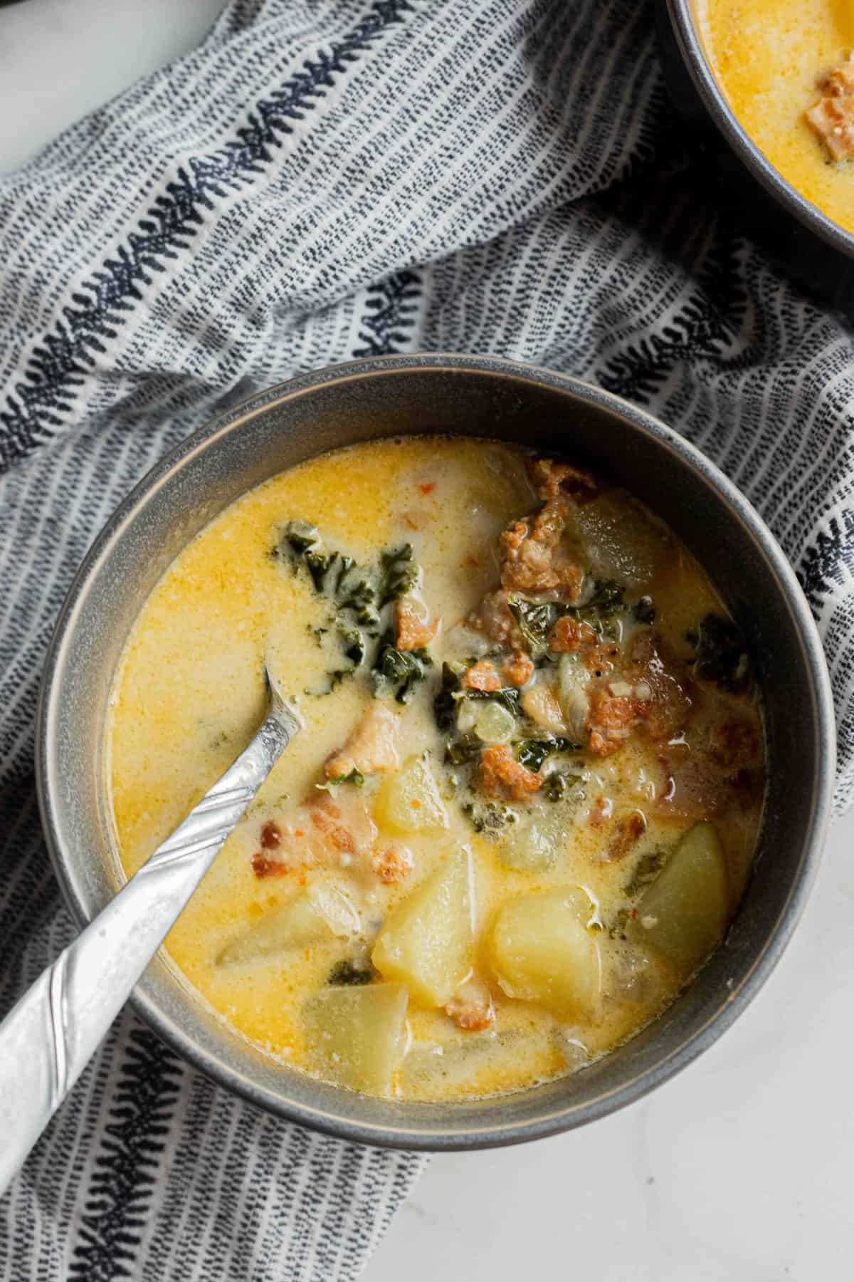 A gray bowl with zuppa toscana soup on a marble surface.
