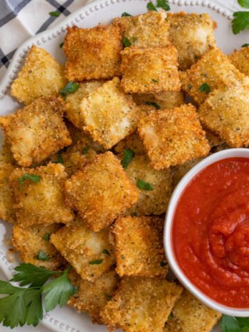 Plate of toasted ravioli with a bowl of sauce.