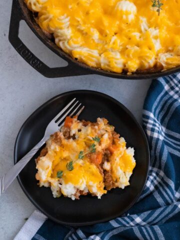A plate of shepherds pie next to a cast iron skillet.