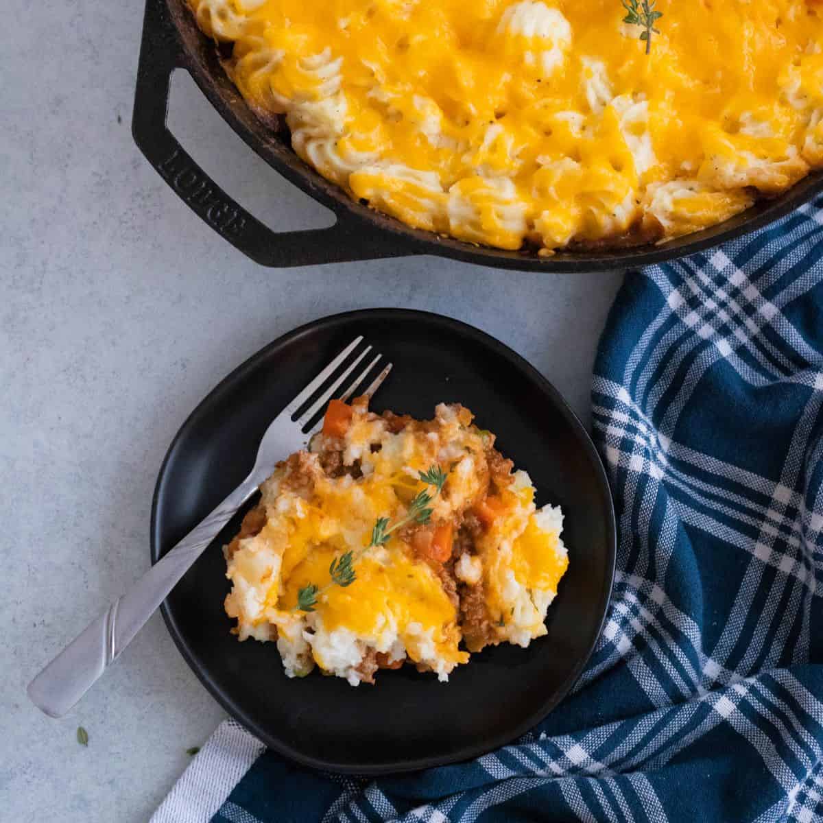 A plate of shepherds pie next to a cast iron skillet.