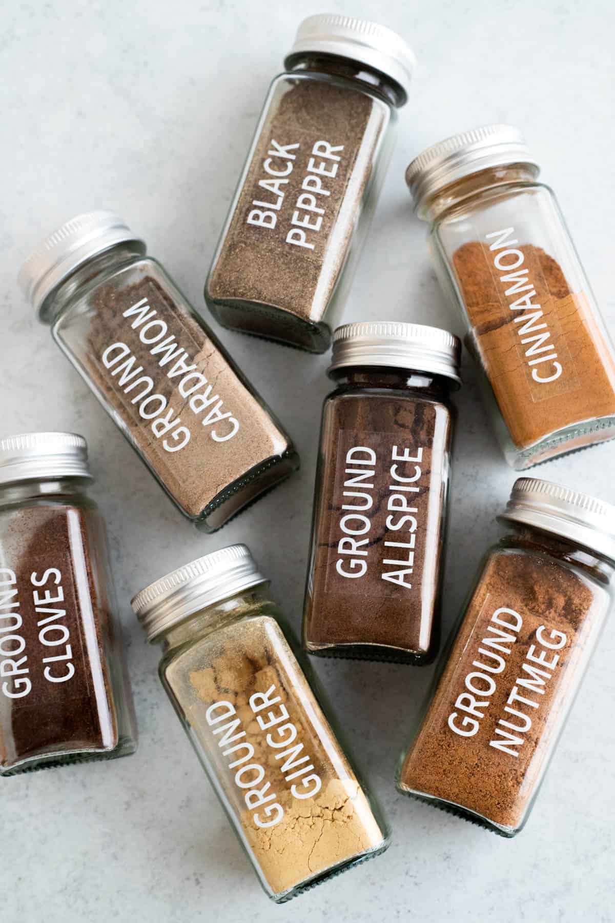 Glass jars of spices laying on a marble surface.