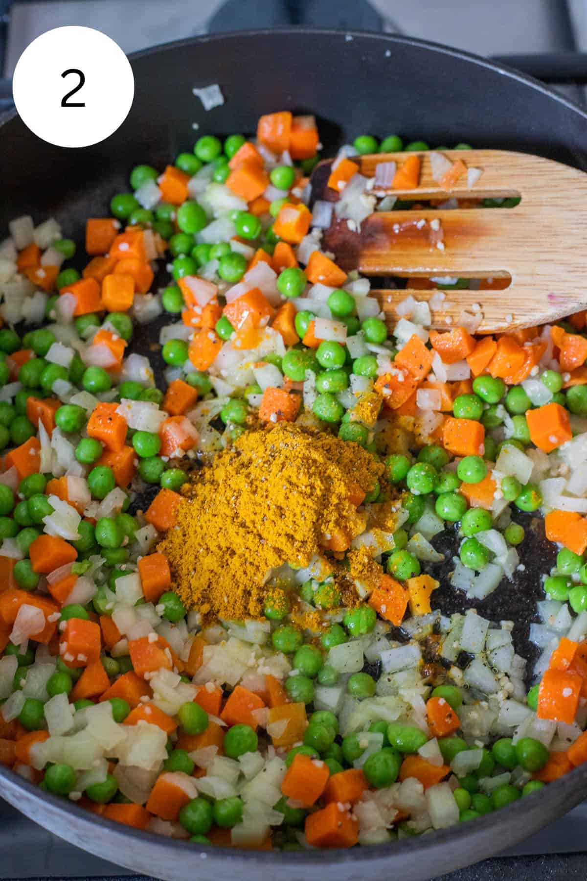 Carrots, peas, and onions, curry powder in a frying pan.