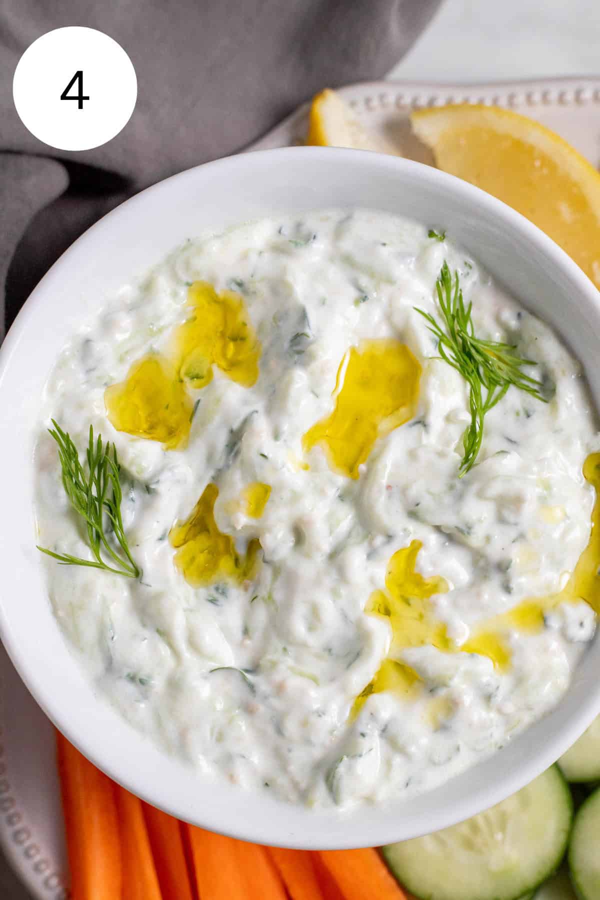 Tzatziki sauce in a white bowl next to veggies.