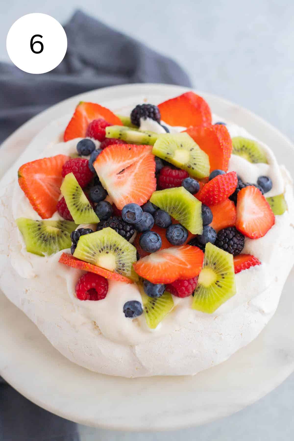 Pavlova topped with berries on a white cake stand.