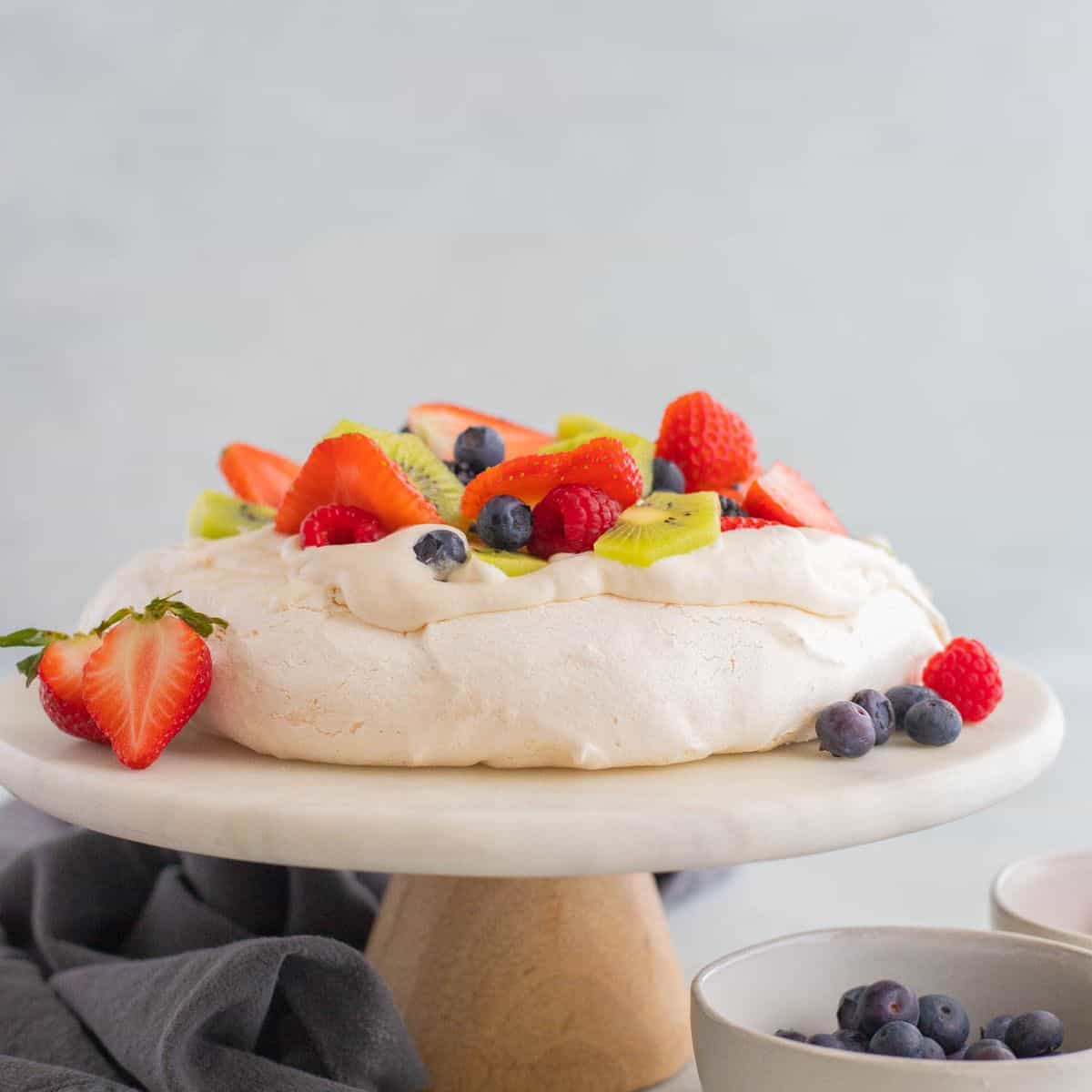 Pavlova topped with berries on a white cake stand.
