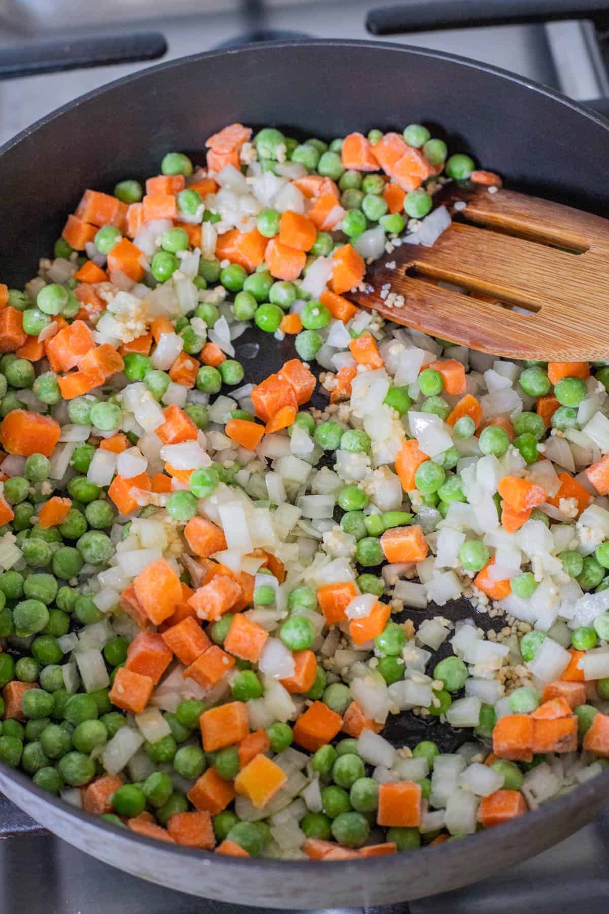 Carrots, peas, and onions in a frying pan.