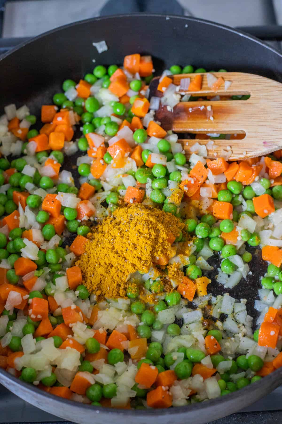 Carrots, peas, and onions, curry powder in a frying pan.