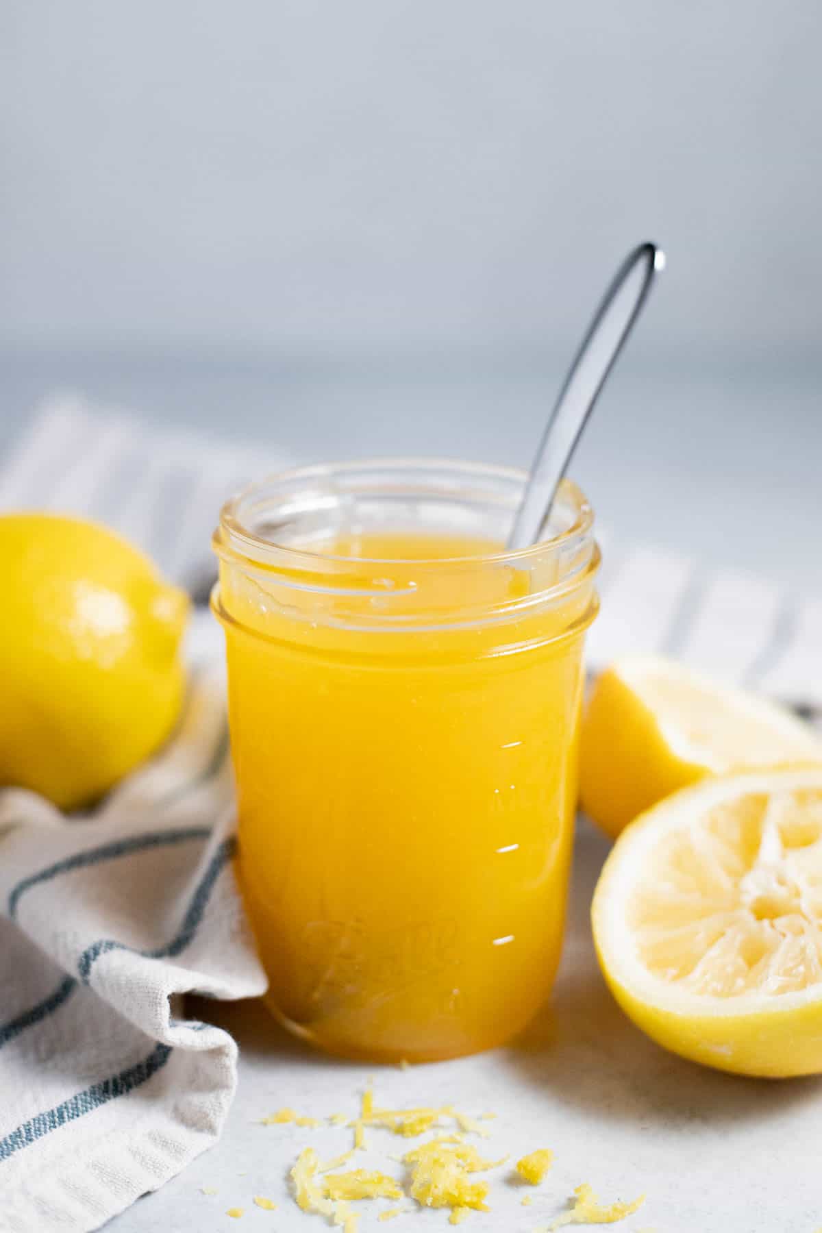 Lemon curd in a glass jar on a gray surface.