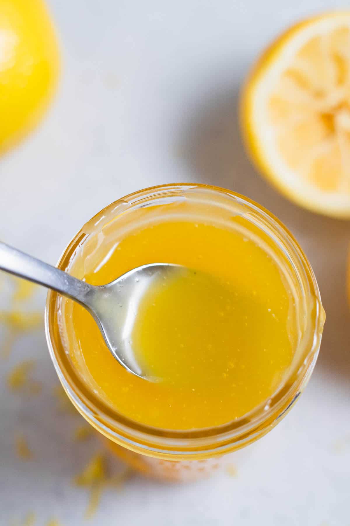 Lemon curd in a glass jar on a gray surface.
