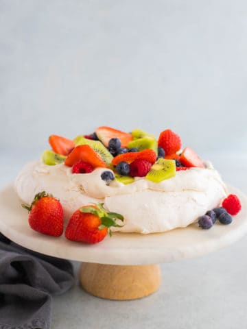 Pavlova topped with berries on a marble cake stand.